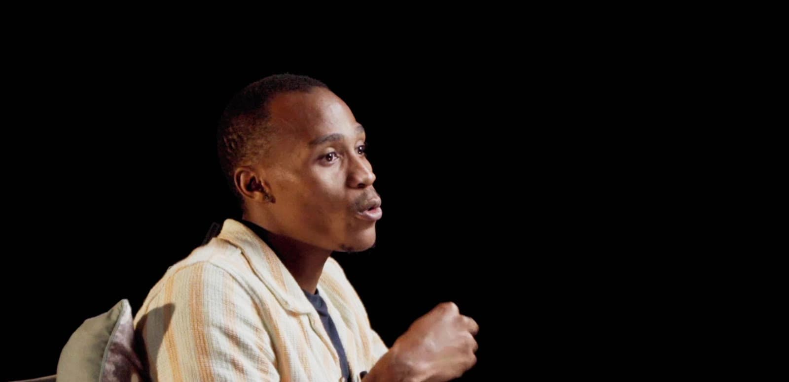 Mpho mid-sentence in interview, lit against a dark background
