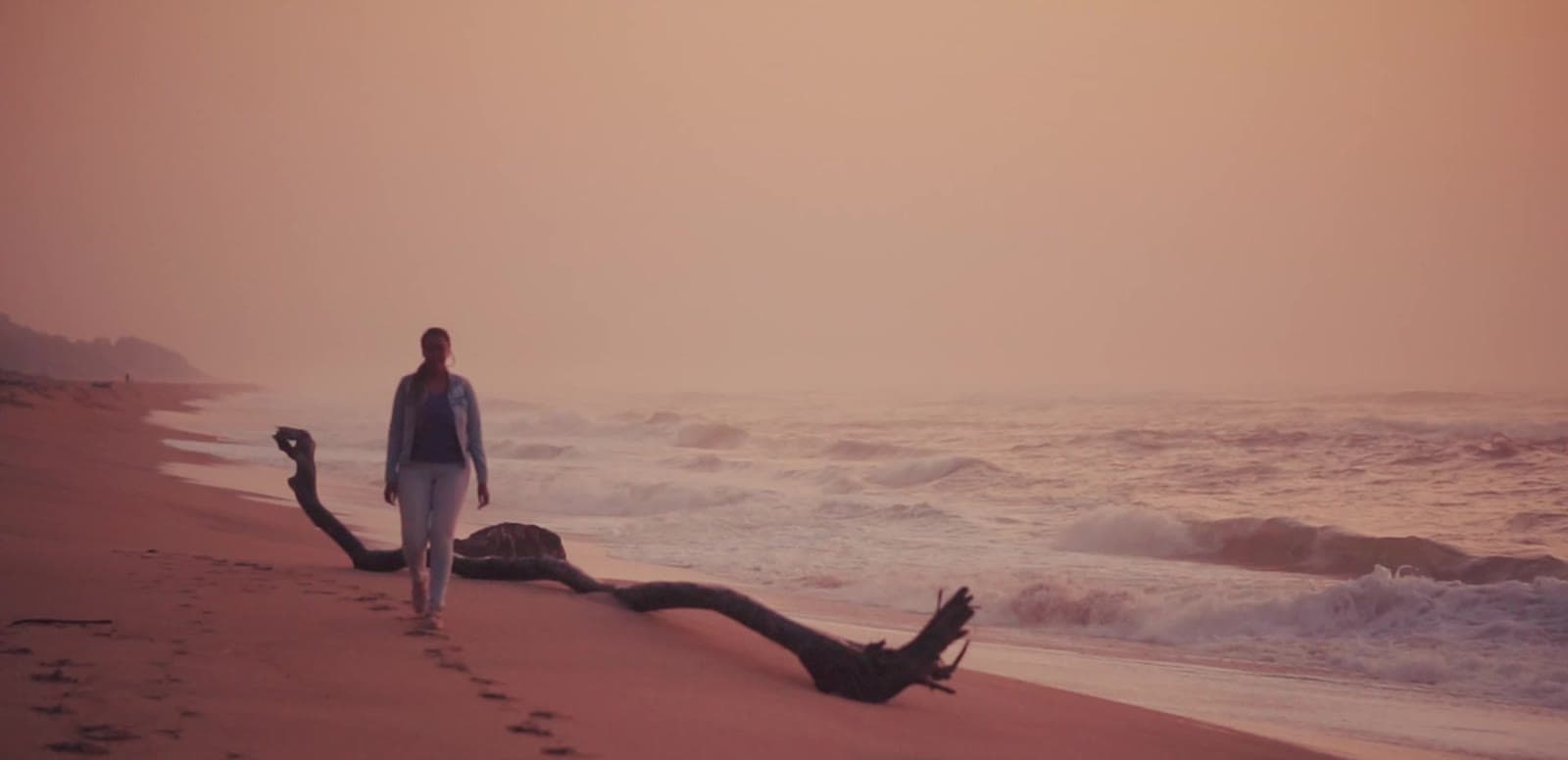 A figure walking the shoreline at dusk